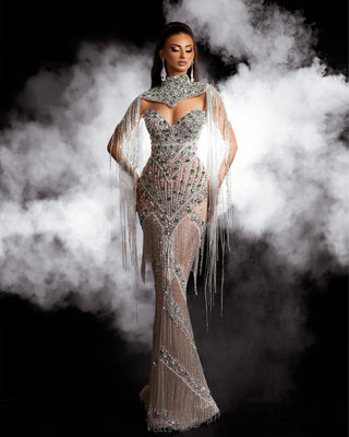 Long silver dress featuring a celestial dance of silver tassels, green and blue crystals, and silver stones. 