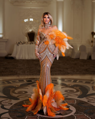 Long orange dress adorned with shimmering crystals and elegant feathers.