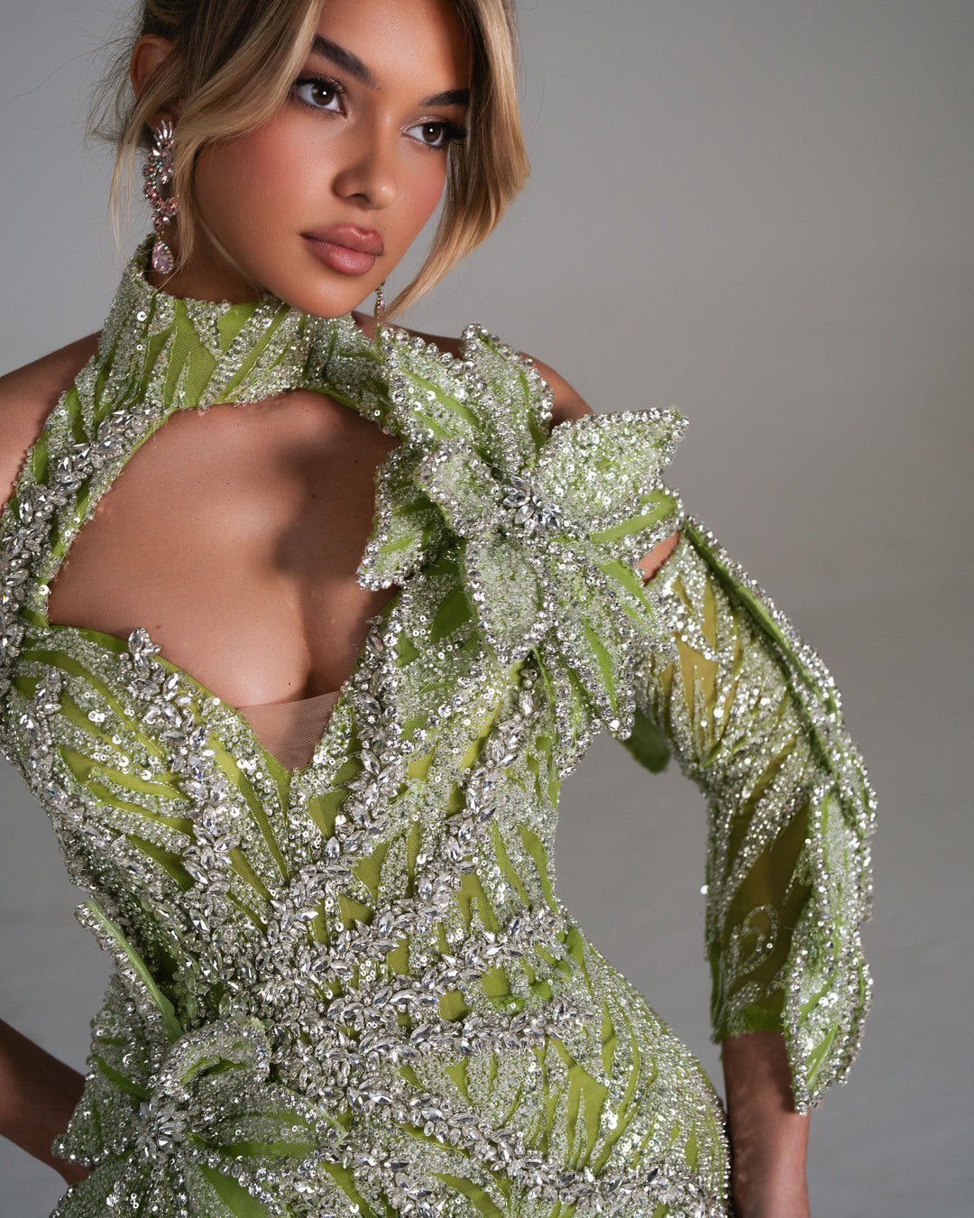 Close-up of a green dress adorned with crystals, featuring a high neckline, open shoulders, and floral detailing.