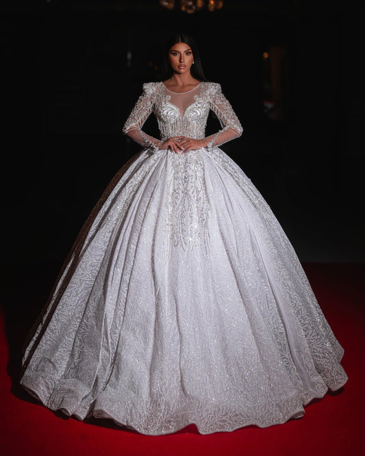 
Bride wearing an elegant white ball gown with long sheer sleeves and intricate embroidery.