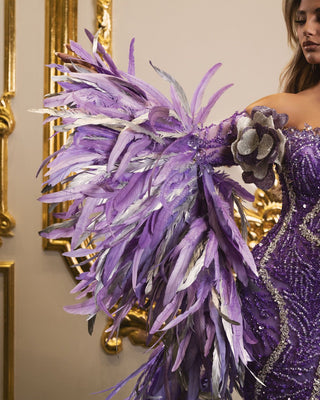 Detailed view of long sleeves adorned with light purple and silver feathers on elegant purple dress