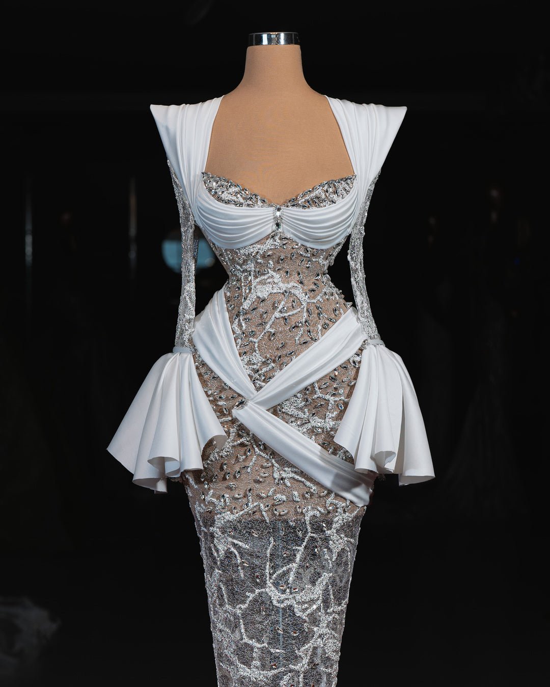 A sparkling bridal gown with lace, crystals, sheer sleeves, and a draped peplum detail.