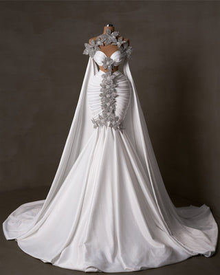 Chic satin bridal gown with crystals, pearls, side cape, and cut-outs.