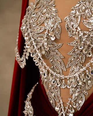 Close-up of the intricate silver embellishments on the bust of a red velvet dress.